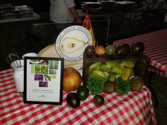 Table display at Dinner for Farmers 2019 featuring fresh fruits and signs for Hammock Greens and Chef David Schwardron.