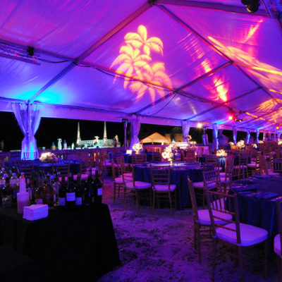 Evening dinner set up under tent on the East Terrace overlooking Biscayne Bay and the Barge. Uplighting in blues and purples with golden palm trees.