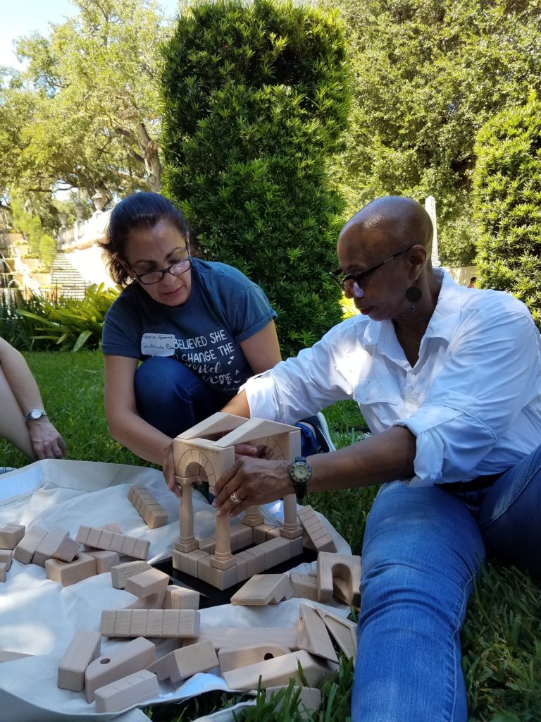 Two adults with a Vizcaya Learning Program Facilitator in the Center Island building a structure with small wooden building pieces.