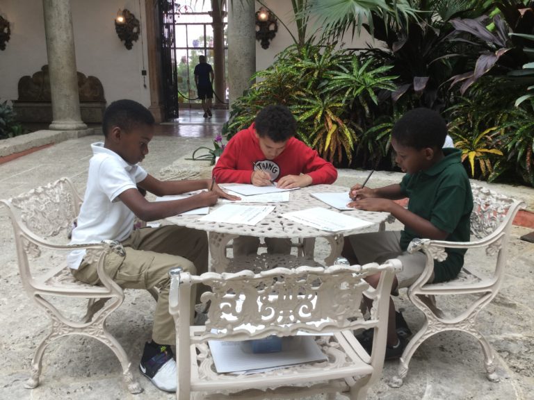 Three children working on a project at a table in the Main House courtyard during a summer camp field trop to Vizcaya.