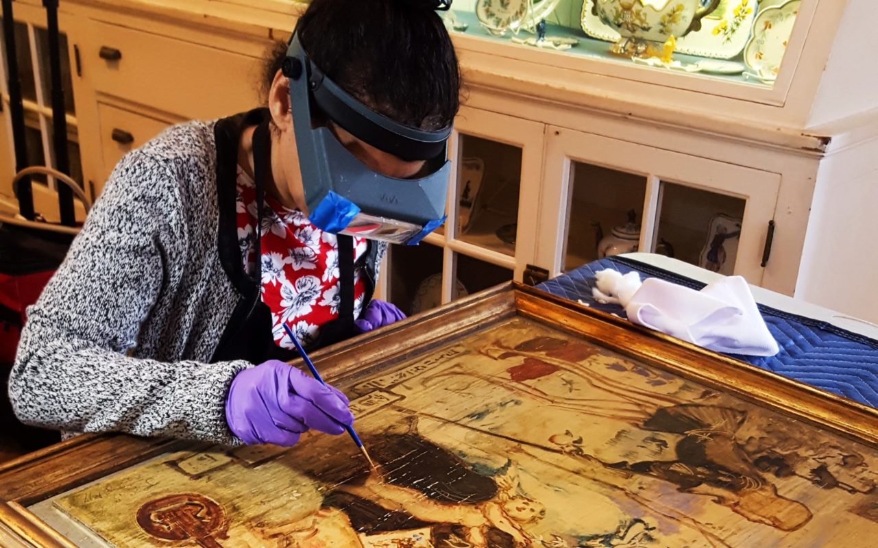 Woman carefully cleaning a painting with a brush and goggles