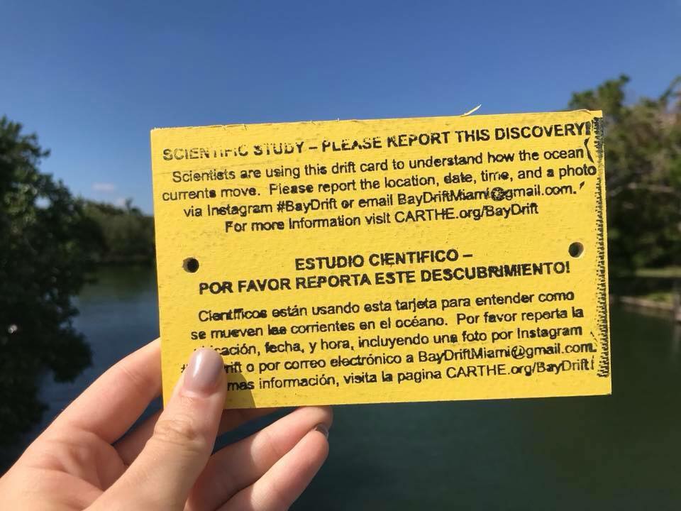 Bright yellow wooden card with writing on it being held up by hand