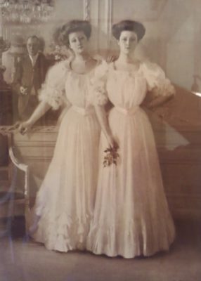 Old photo of two women posing together in long white dresses