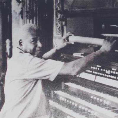 Black and white photo of Eustace Edgecomb changing the music roll in the player organ.