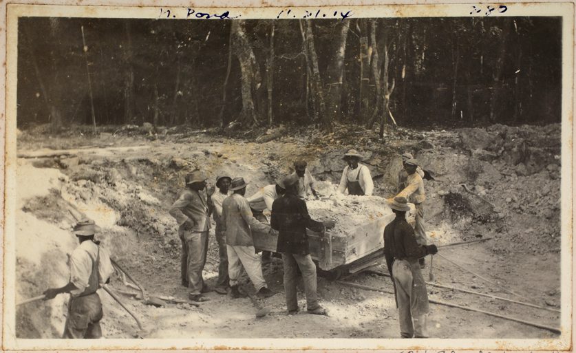 Black and white photo of eleven men around a trolley of gravel.