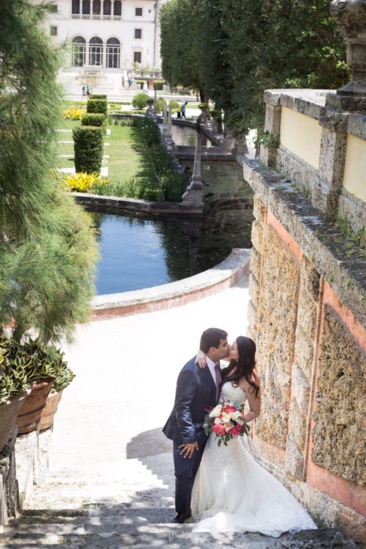 A bride and groom kissing on the steps of a mansion.