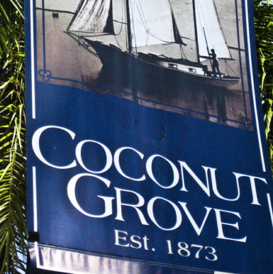 Pole sign that reads Coconut Grive est. 1873 and shows an archival photo of a sailboat
