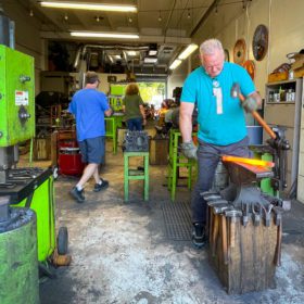 Blacksmith shop featuring a man with white hair working a piece of hot metal on an anvil