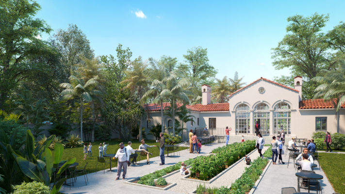 The back entrance to Vizcaya's Superintendent's House, a coral-colored building with barrel tile roof and three large windows and two chimneys. People are walking around or sitting at black tables with a vegetable garden running down the middle of the space. There are palm trees and other large trees as well as a grassy lawn.