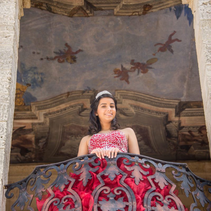 Quinceañera Teen girl in red ball gown standing in a balcony