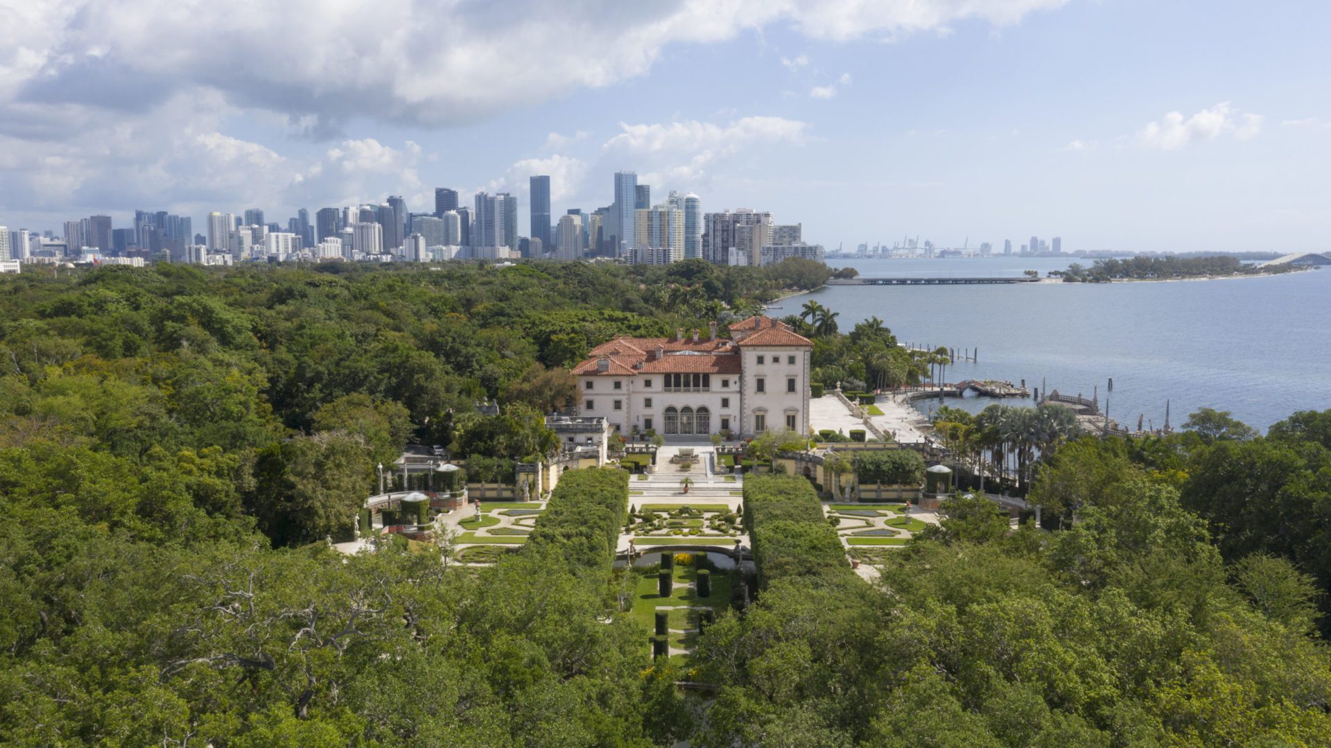 Aerial photo of Vizcaya's Main House surrounded by lush formal Italian gardens and views of downtown Miami in the background. Photo by Robin Hill