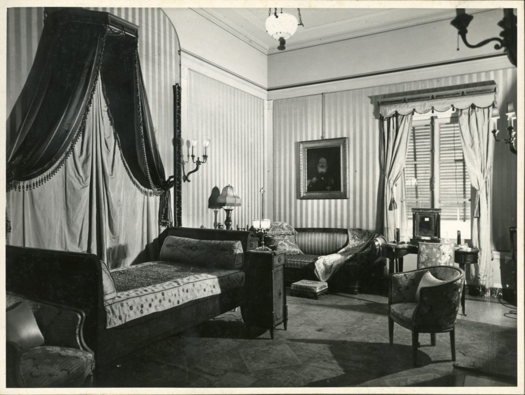 Historic black-and-white photo of the Manin bedroom showing a canopy bed, couch, drapes and other furnishings.