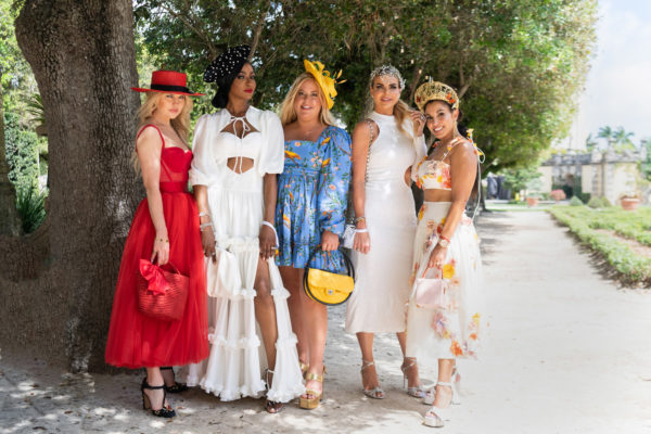 A group of ladies in colorful attire and hats poses for photos in the gardens.