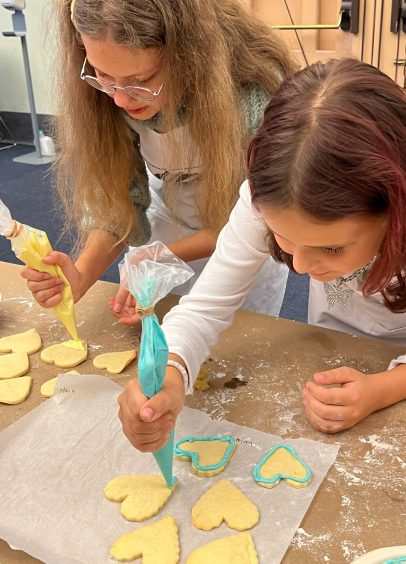 A woman with long hair and a child decorating heart-shaped sugar cookies with blue and yellow icing.