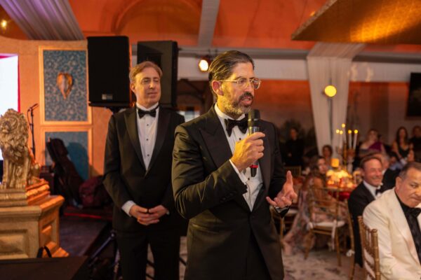A man in a tuxedo speaking into a microphone at the Vizcaya Ball.