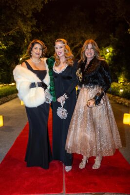 Three women standing on a red carpet at the Vizcaya Ball.