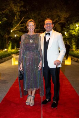 A man and woman, dressed elegantly for the Vizcaya Ball, stand atop a stunning red carpet.