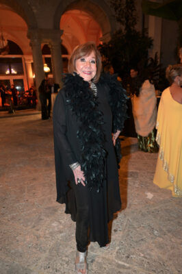 A woman wearing a black dress with a black feathered hat graces the Vizcaya Ball, exuding elegance and style.