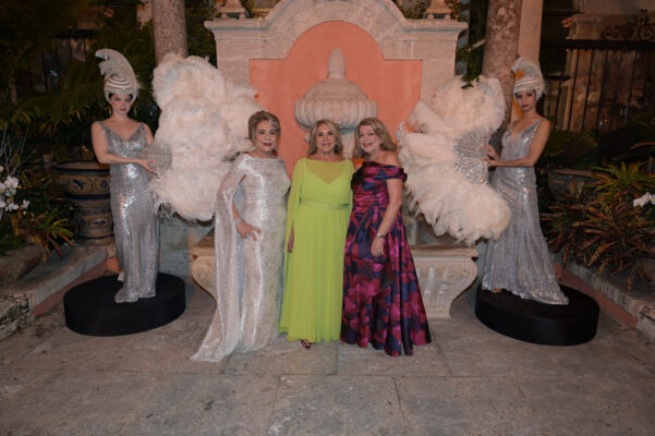 Three women attending the Vizcaya Ball posing for a photo in front of a fountain.