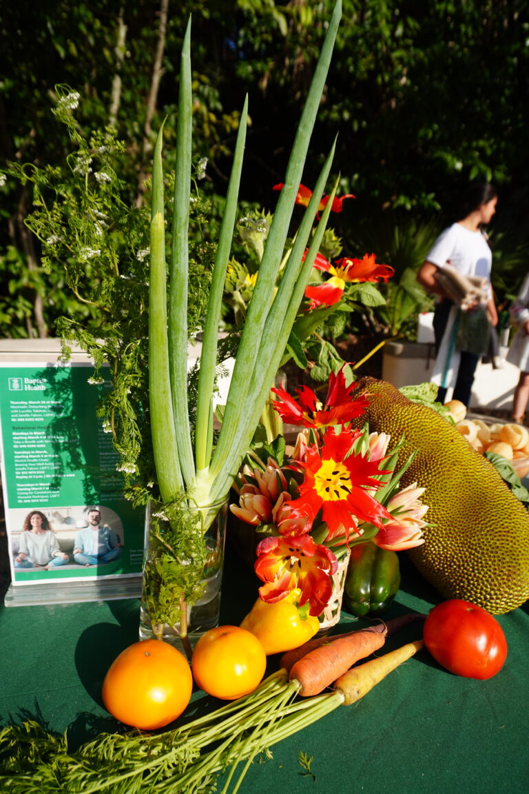 A vibrant display of fresh vegetables and flowers on a table with informational materials in the background.