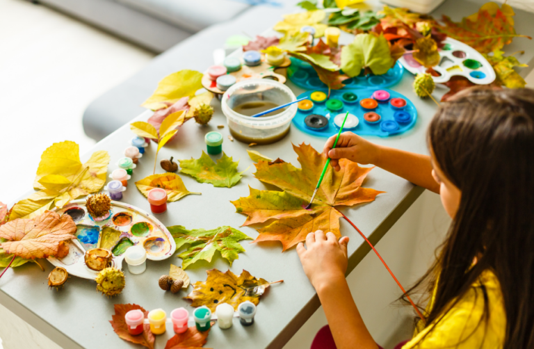 A child paints a leaf among scattered autumn leaves and art supplies on a table during programs for students at Vizcaya.