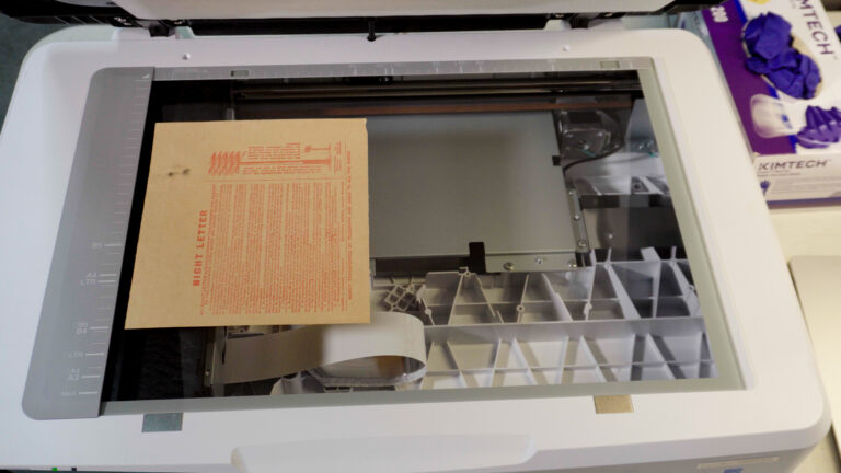 Open flatbed scanner with a brown sheet of paper containing red text placed on the glass, ready to be scanned.