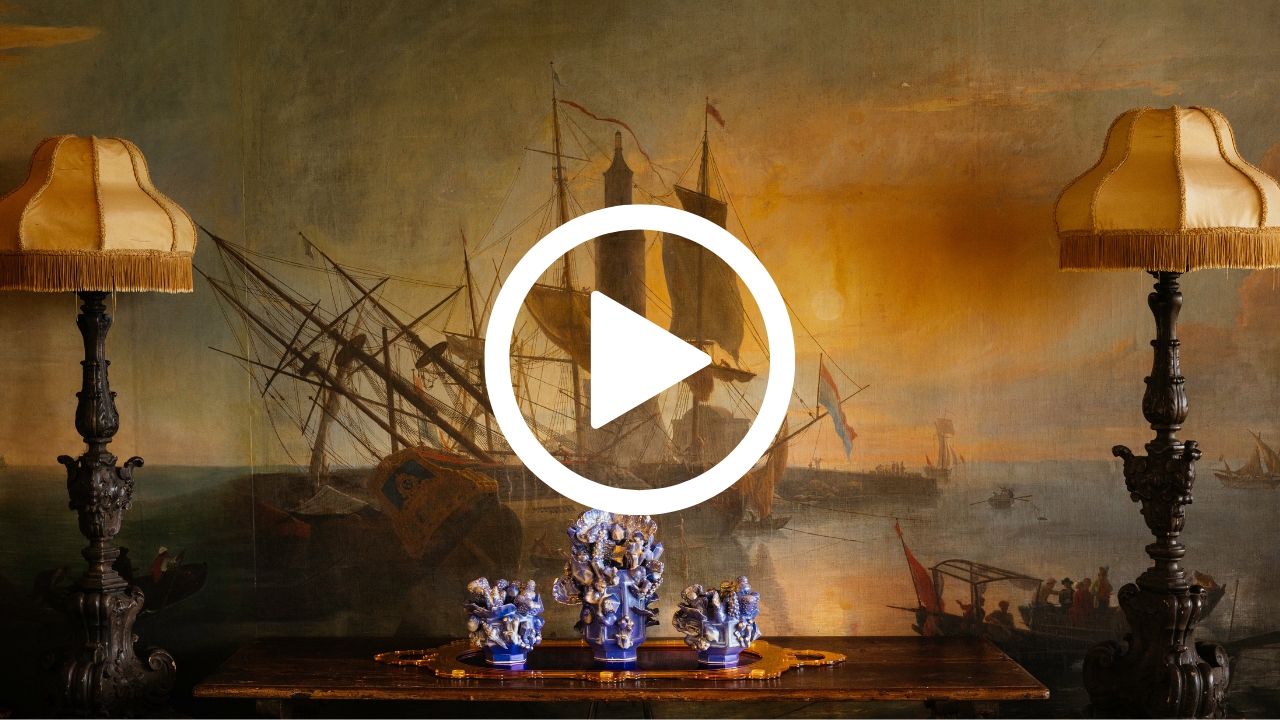 Ornate table with blue porcelain figurines between two lamps, set against a wall mural depicting historic sailing ships at sunset.