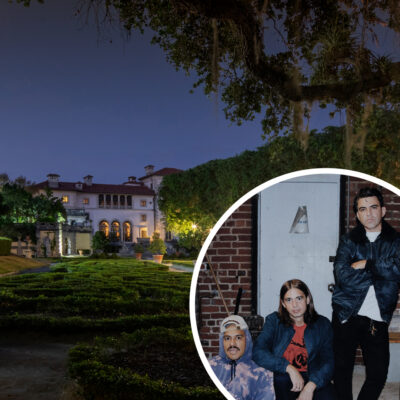 A large mansion with manicured gardens at night; in the foreground, an inset shows three people posing in front of a brick wall and door.