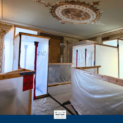 Temporary plastic and wood enclosures are set up inside an ornate room with decorative ceilings, likely to protect the area during construction or renovation work.