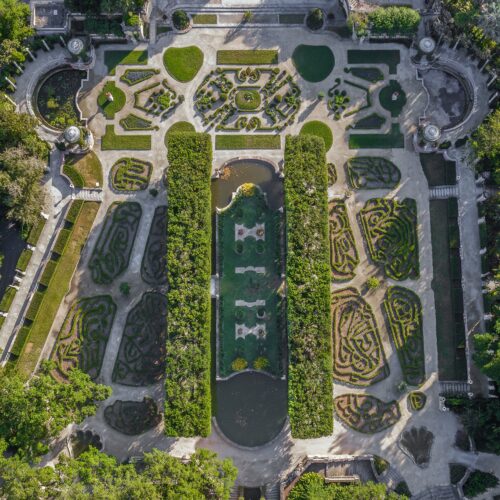 Aerial view of a formal garden with symmetrical hedges, geometric pathways, ponds, and neatly trimmed bushes.